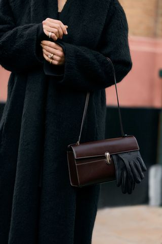 Woman wears black coat and brown Savette handbag over her arm