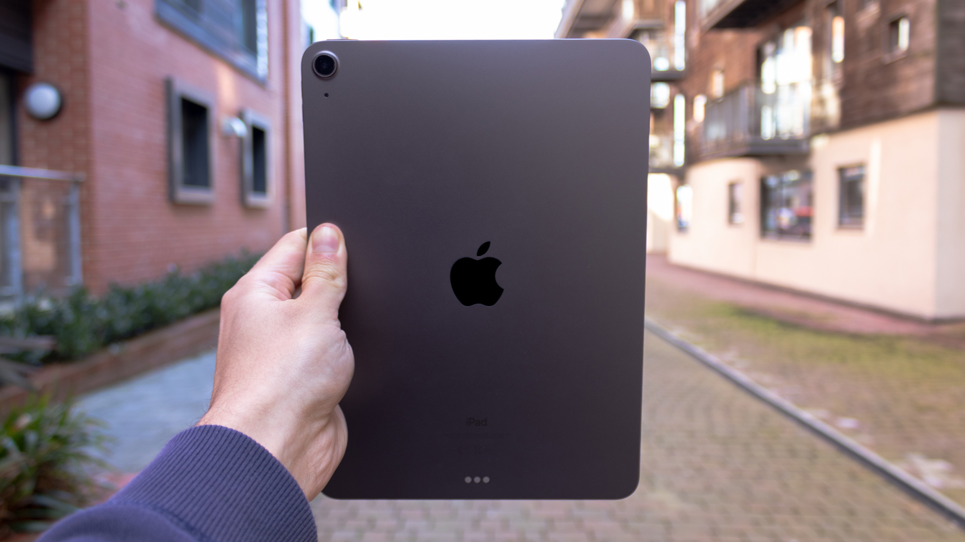 A photograph of the rear of an Apple iPad Air being held up outside