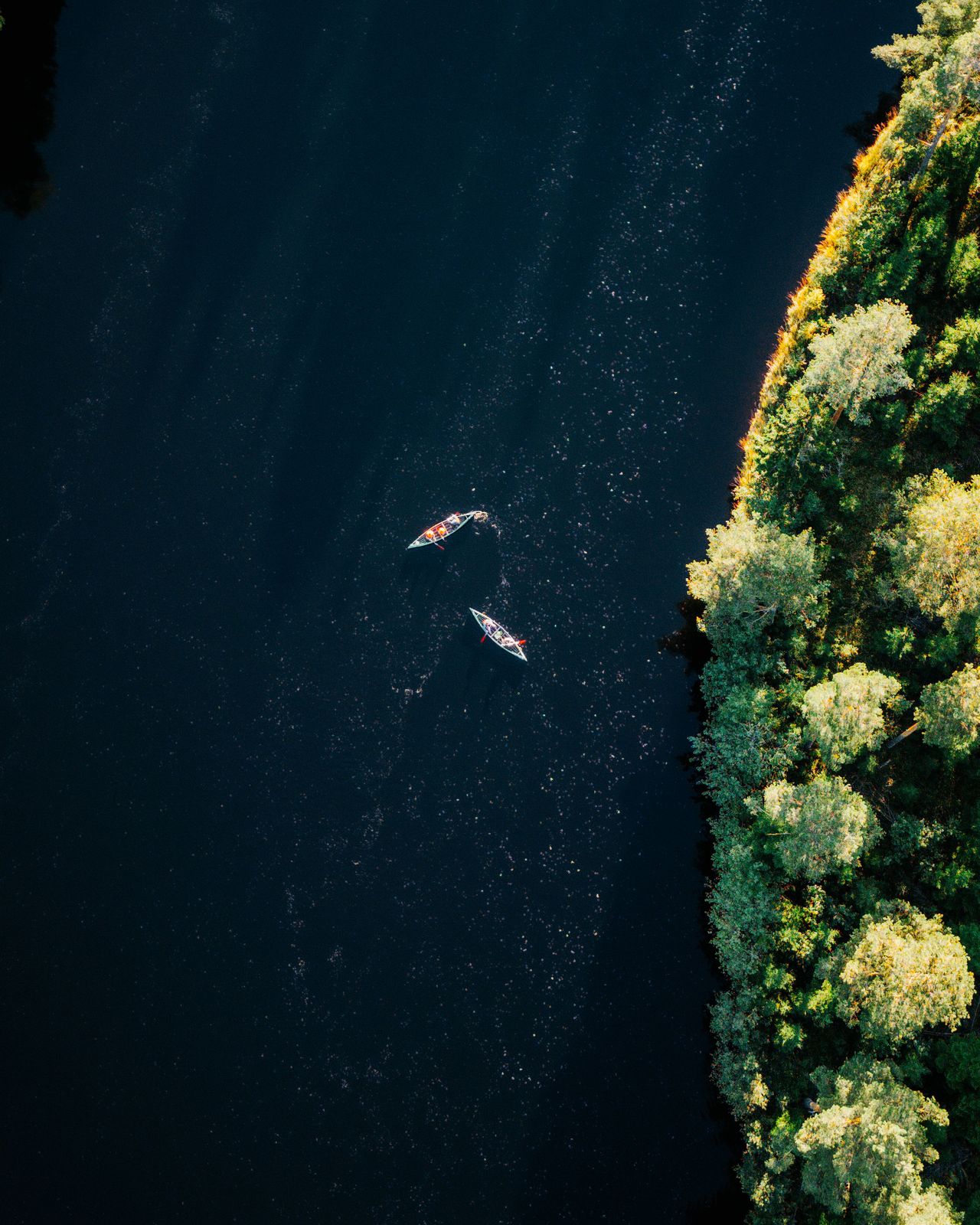 An aerial view of a sun-lit canal with two people kayaking in it.