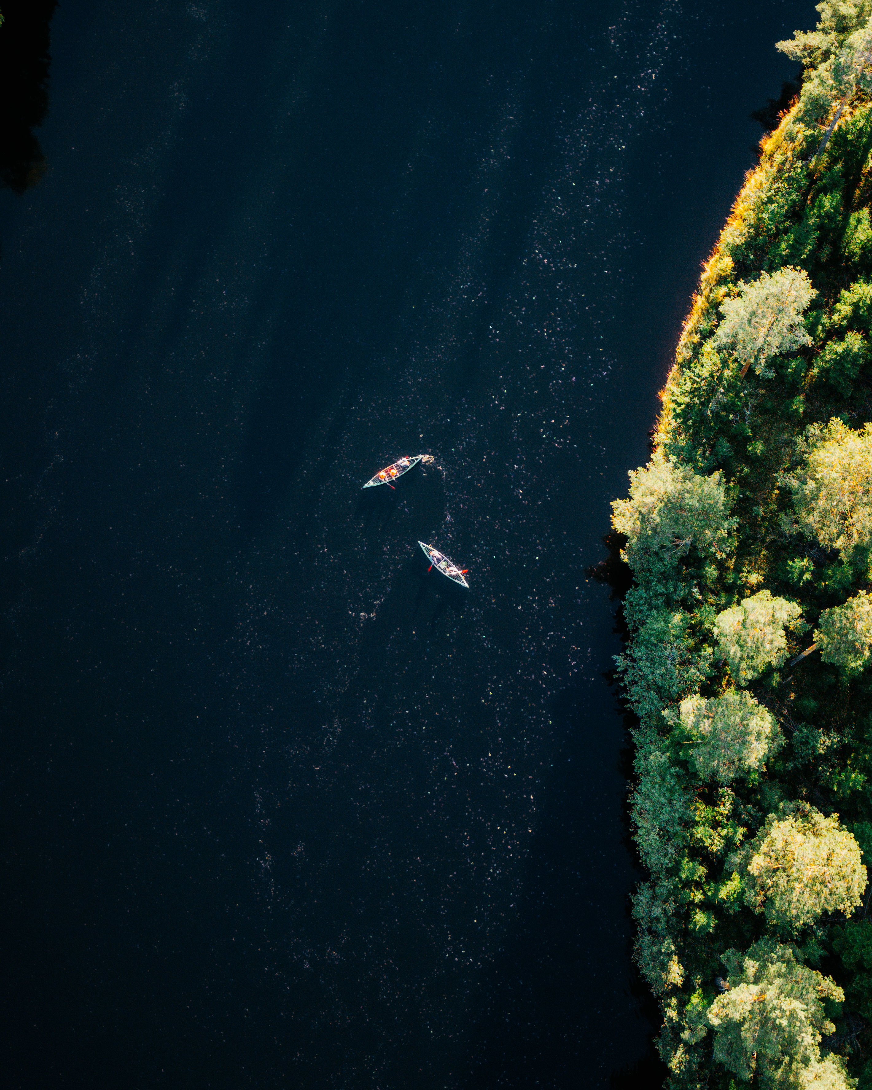 An aerial view of a sun-lit canal with two people kayaking in it.