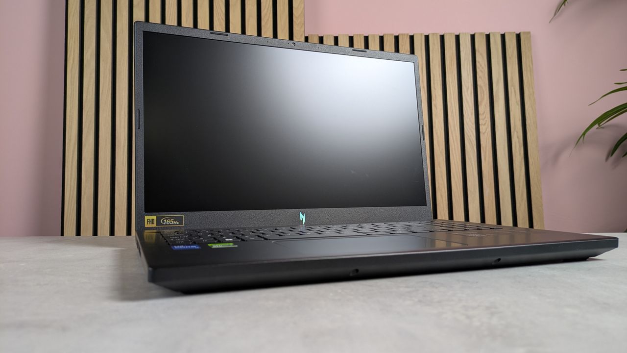 Acer Nitro V 15 open on desk with wooden panels, plant, and pink wall in background