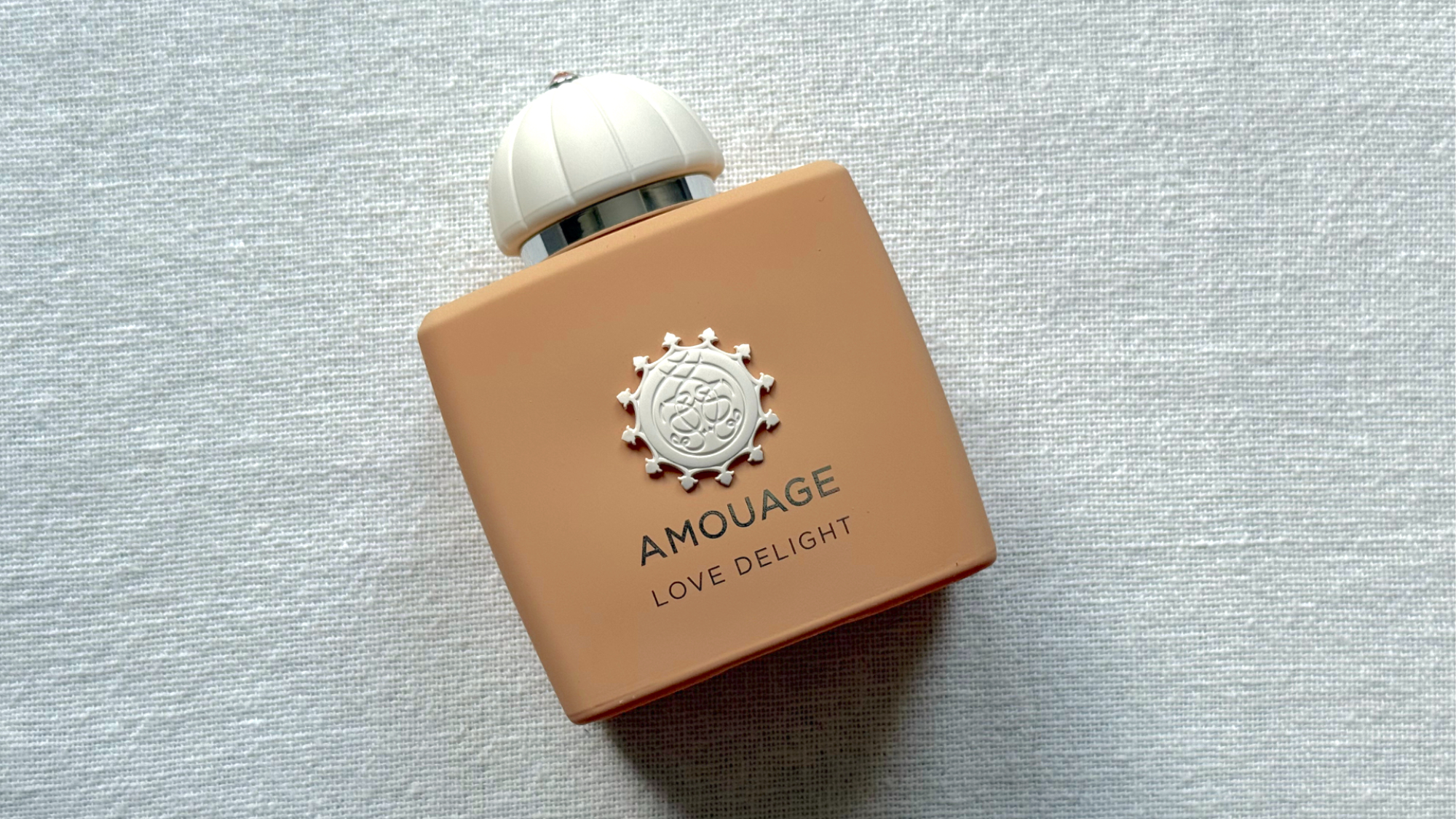 A bird's eye view image of the Amouage Love Delight perfume set against an off-white linen background