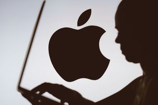 Apple logo is seen in the background of a silhouette of a person using a notebook