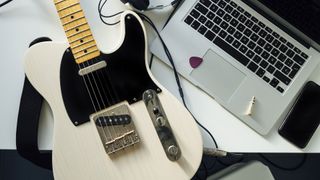 Telecaster style guitar and a laptop laid on a desk