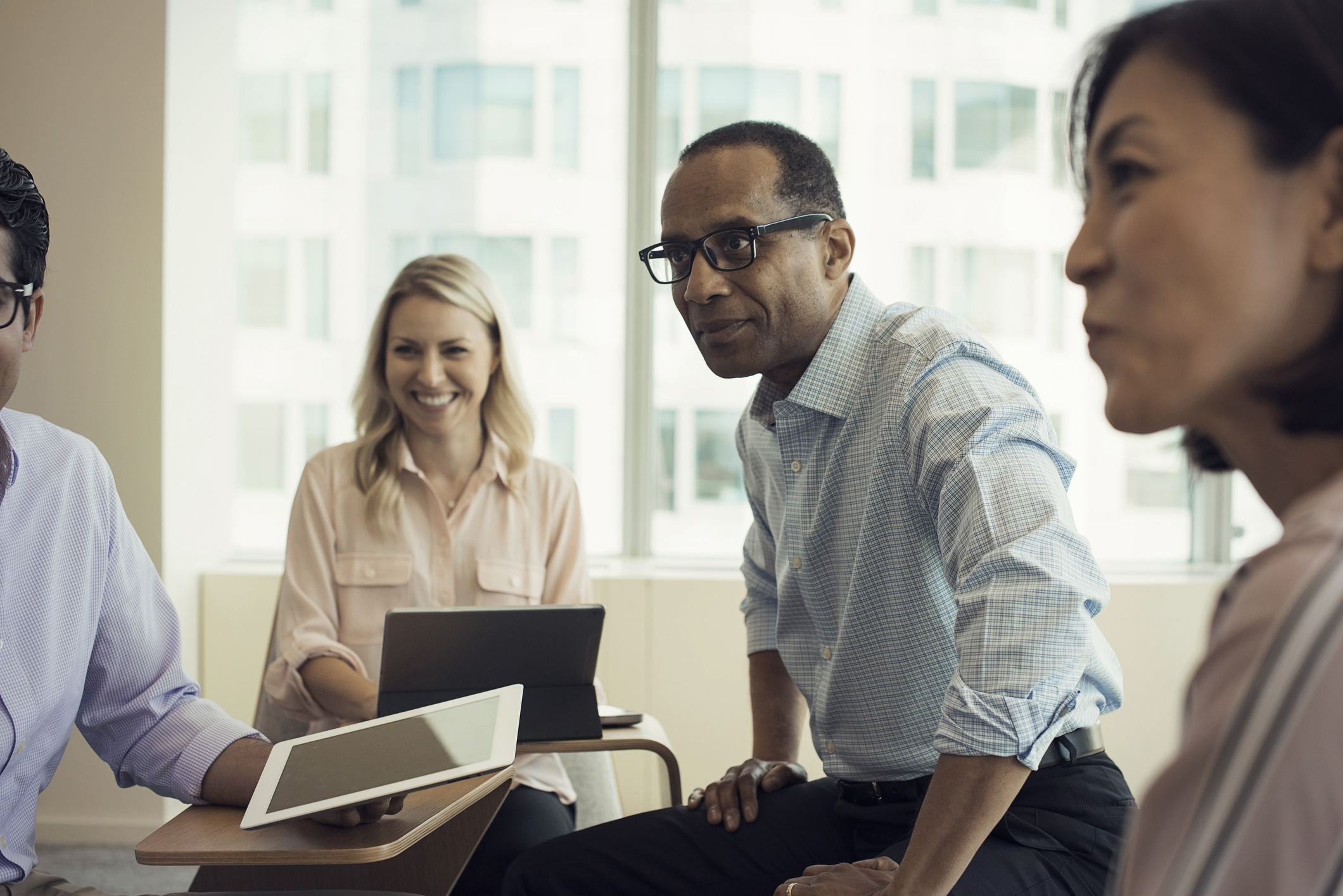 Four office workers of different ages smile during a meeting.