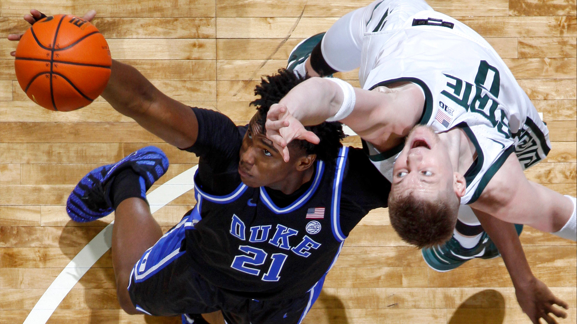 Two players reach out for a basketball during a NCAA college game in East Lansing, USA