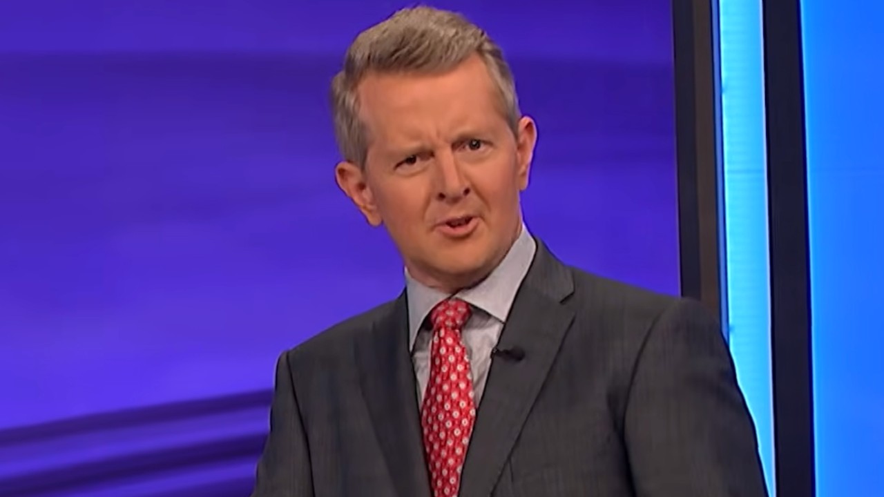 Ken Jennings talking to the camera and wearing a red tie with a white diamond pattern. 