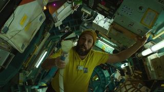 An astronaut in a yellow shirt floats in zero-G