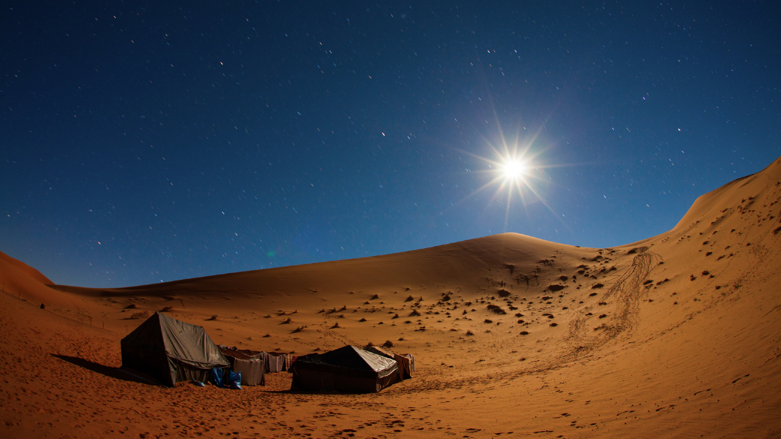 A pair of tents sit in the Sahara desert in Morroco with the Sun beating down on them
