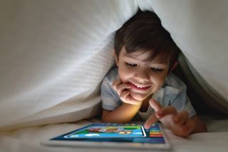 child using tablet under duvet