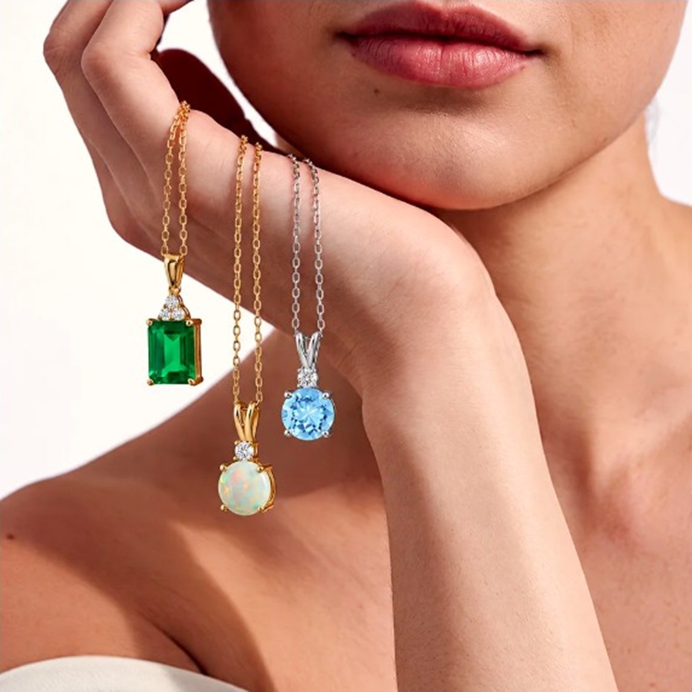 A close up shot of a model holding their hand to their chin while holding 3 Angara necklaces with the stones hanging down
