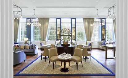 Waldorf Astoria lounge with light purple sofas, beige dining chairs, beige rug trimmed with purple, and purple framed mirrors