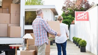 mature man and woman carrying cardboard boxes into their new home