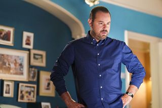 Mick Carter in a blue shirt with his arms on his hips in EastEnders 