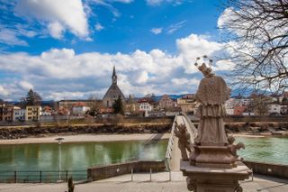 a statue and a bridge over a river into a tow with a church with blue sky