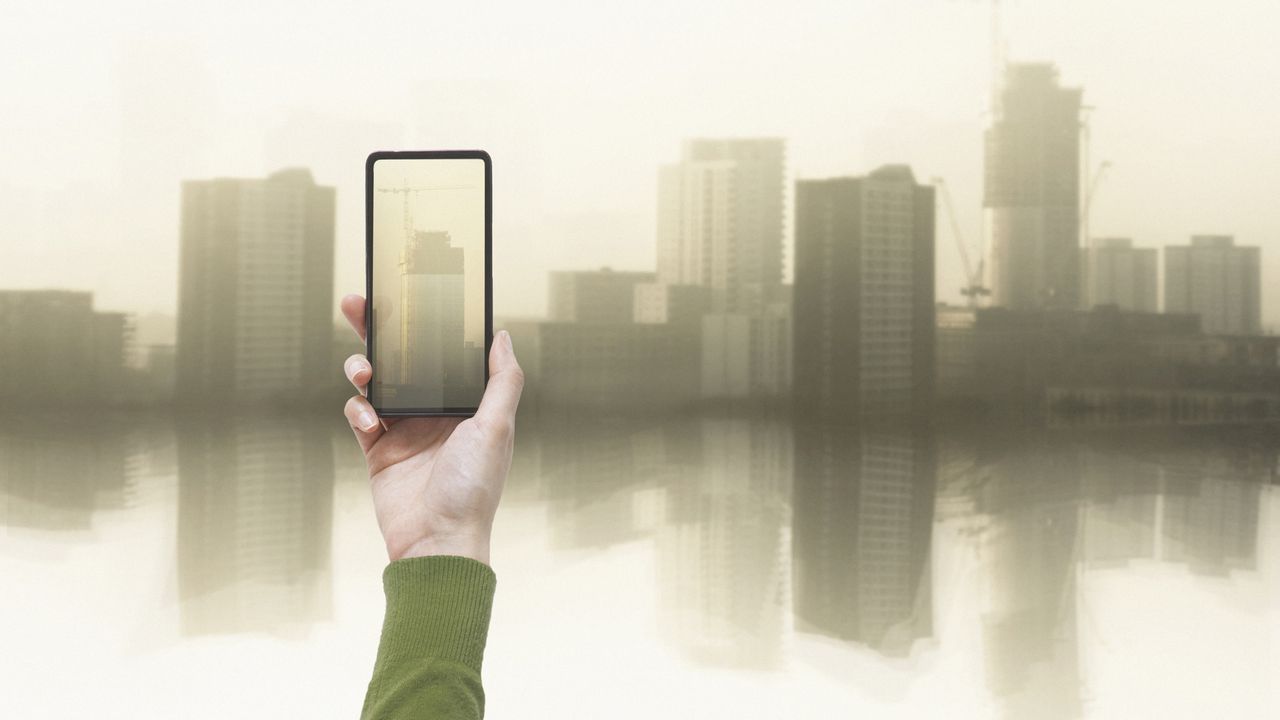 A person takes a photo of a skyscraper from a distance.