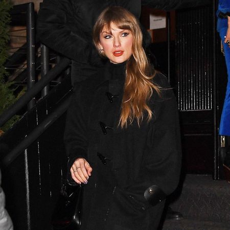 Taylor swift wears a black wool coat, black sheer tights, and black knee-high boots.