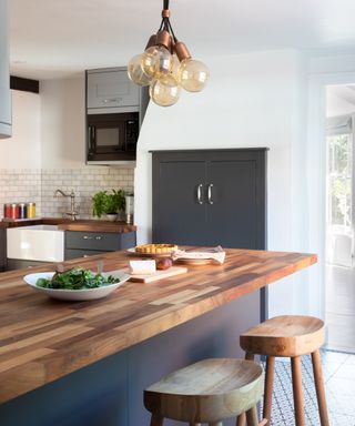 kitchen with grey doors on a cupboard built into chimney breast, large island with wooden top and cluster bulb pendant light above