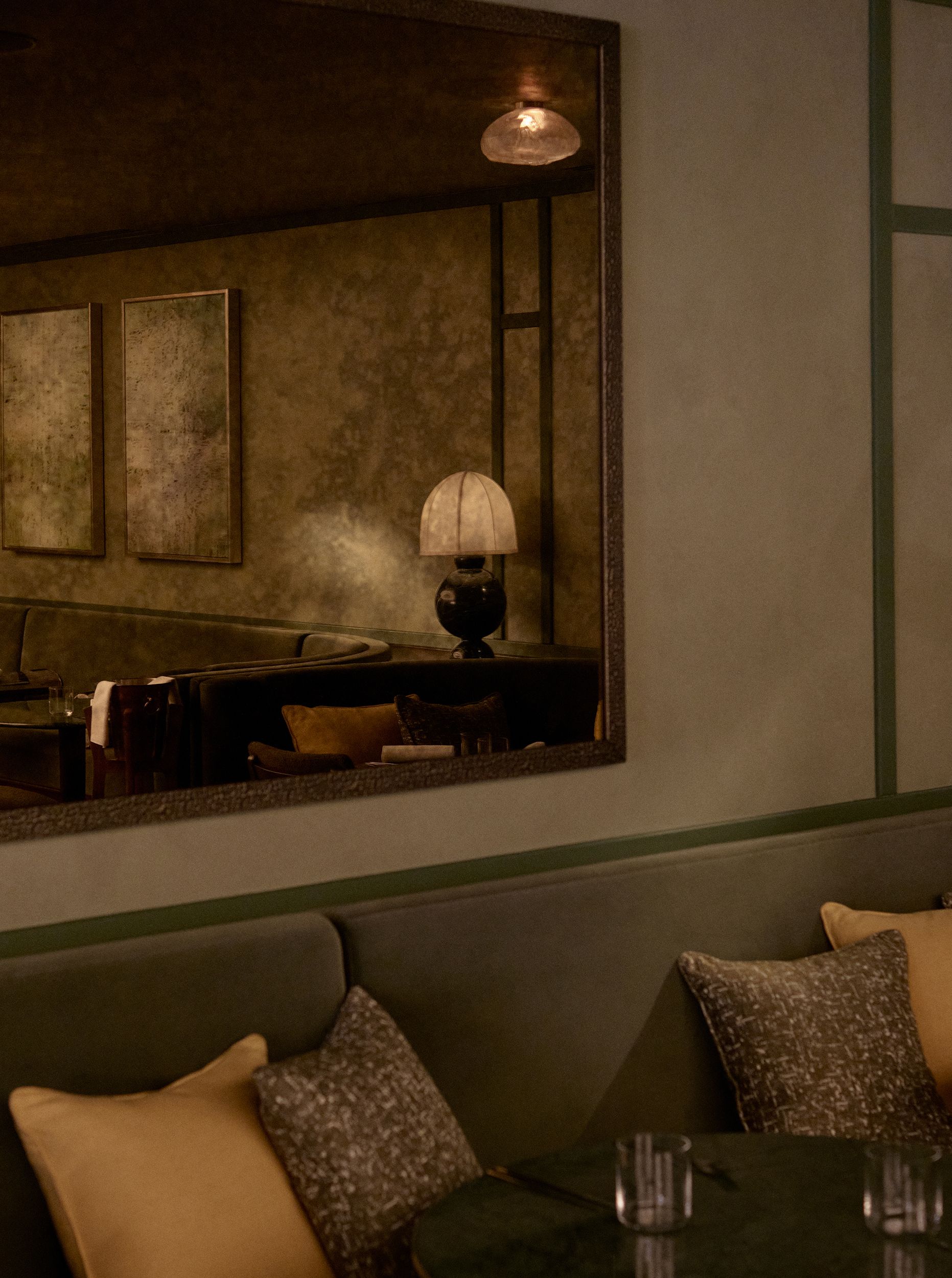 A warmly decorated, vaguely Art Deco-reminiscent hotel features plush textiles in green tones, beige walls, and sculptural lighting.
