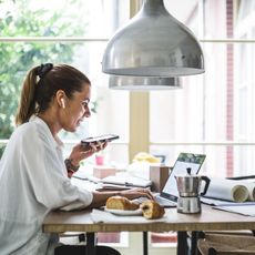 smiling female entrepreneur using laptop while talking through smart phone at home office