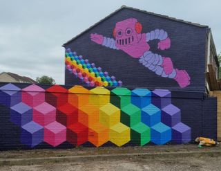 The side of a house painted in rainbow colours and a pink robot