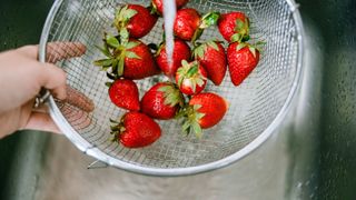 Strawberries being washed under a tap in a sieve