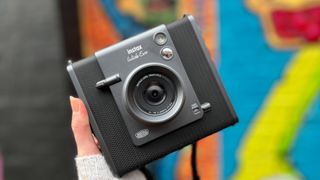 A hand holds up the Fujifilm Instax Wide Evo