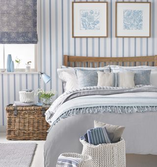 Country-style bedroom with blue-striped wallpaper, wicker hamper as bedside table and wooden bed