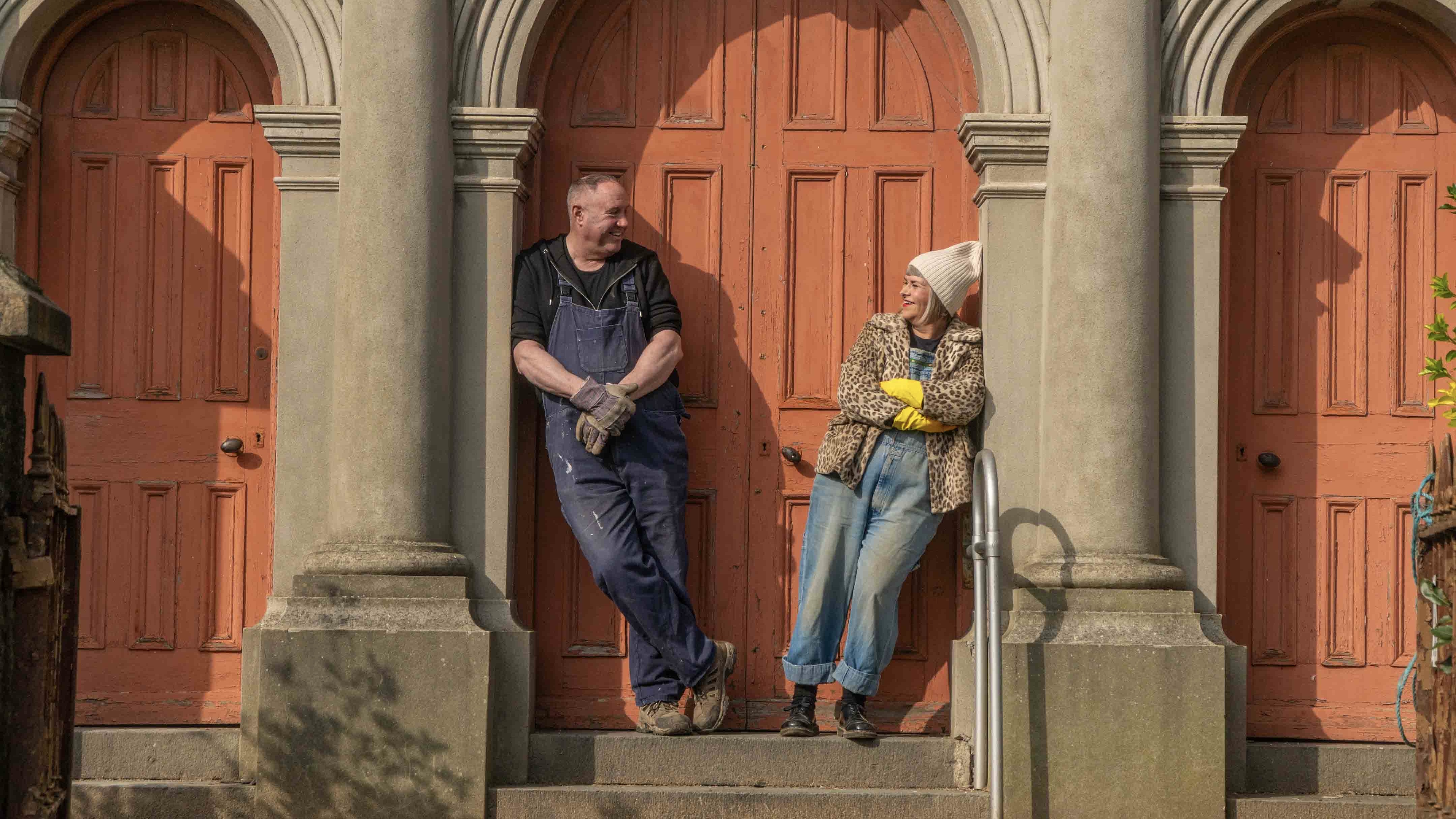 Keith Brymer Jones and Marj Hogarth in overalls stand in the doorway of their chapel in Our Welsh Chapel Dream
