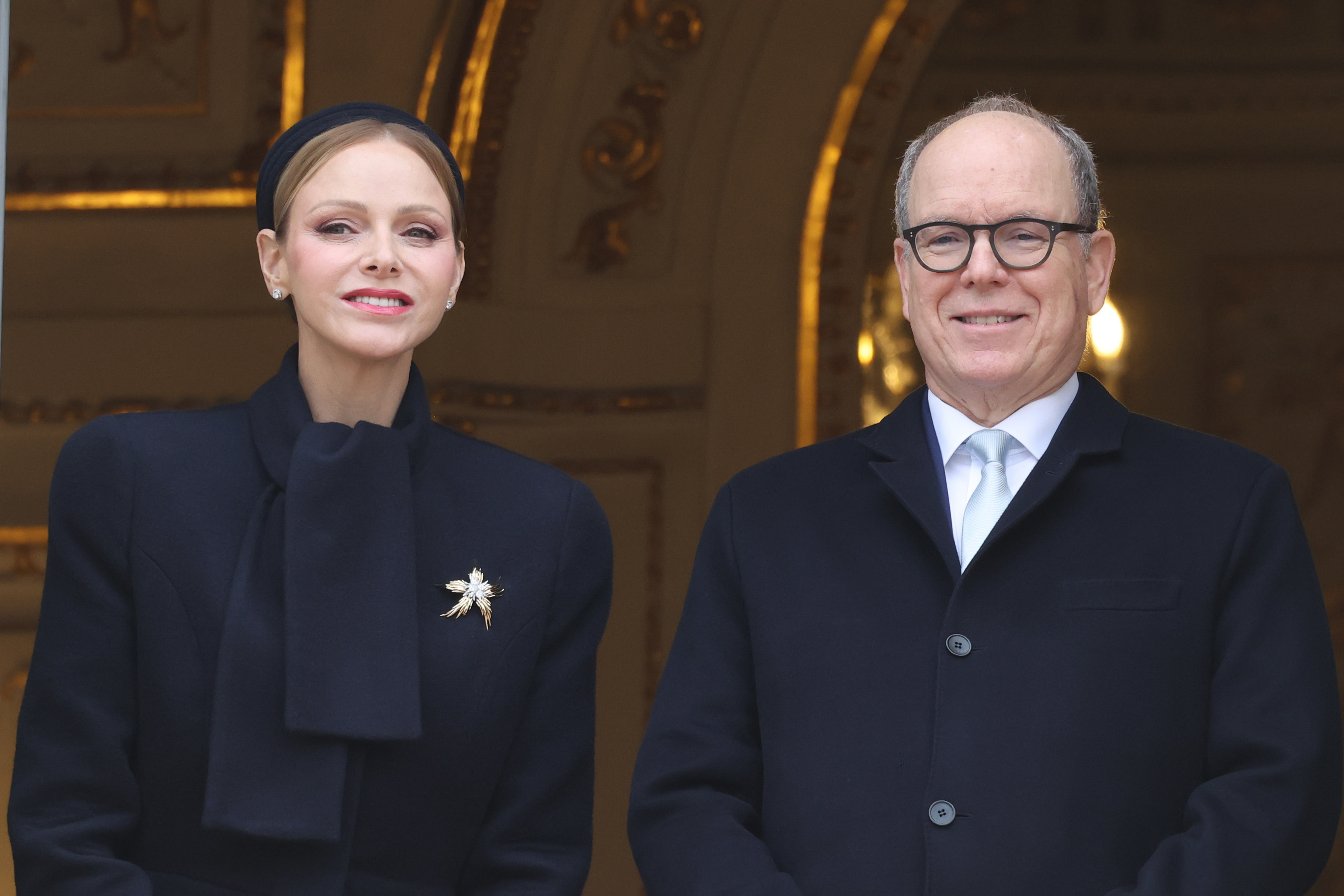 Princess Charlene and Prince Albert standing on a balcony in navy coats