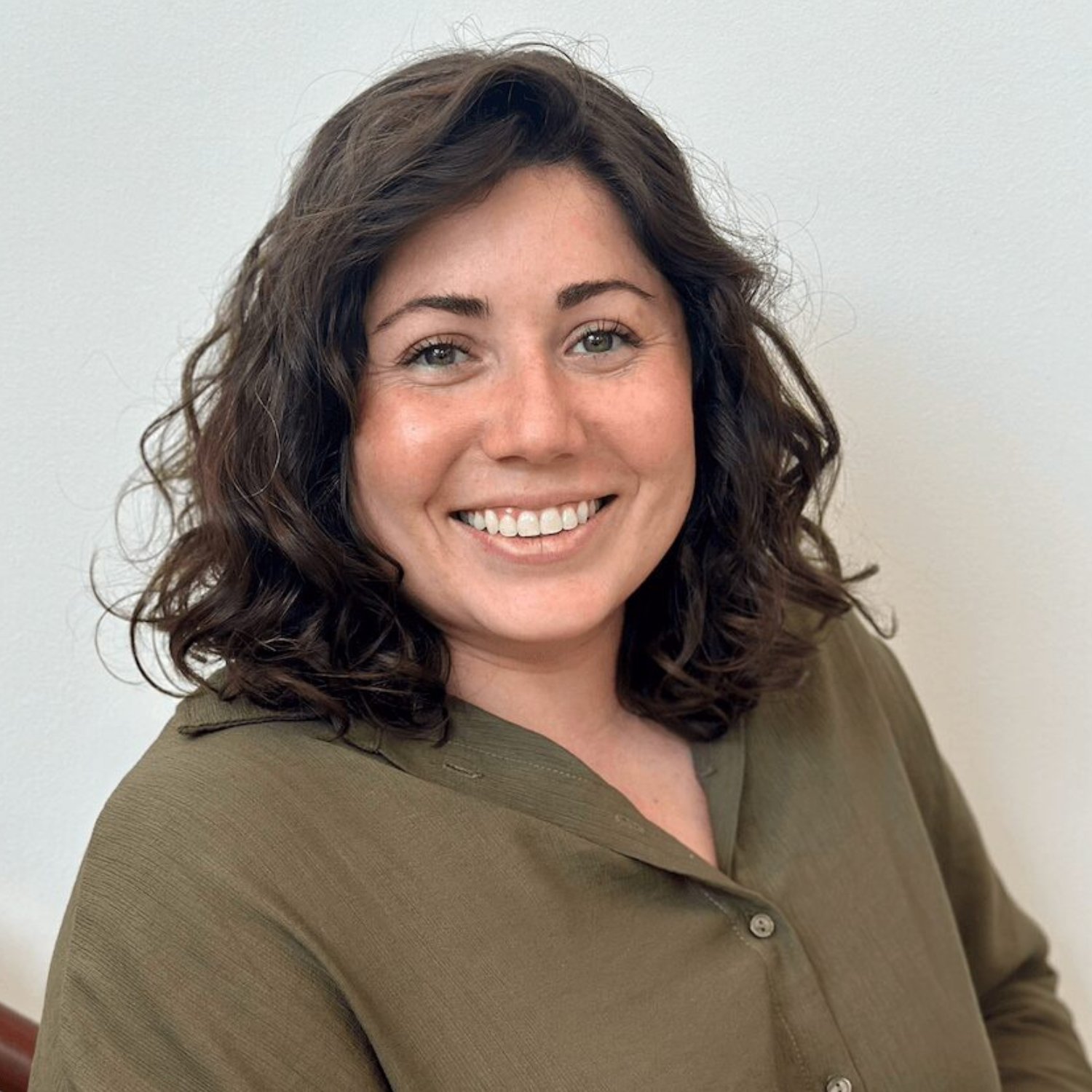A headshot of a woman in a dark green button down with short curly hair