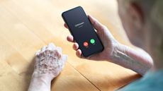 An older woman looks at her phone, which says "Unknown Caller" on the screen.