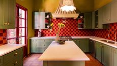 Image of a kitchen that has olive and yellow green paint on the walls and cabinets with a red orange and magenta red tile and trim. 