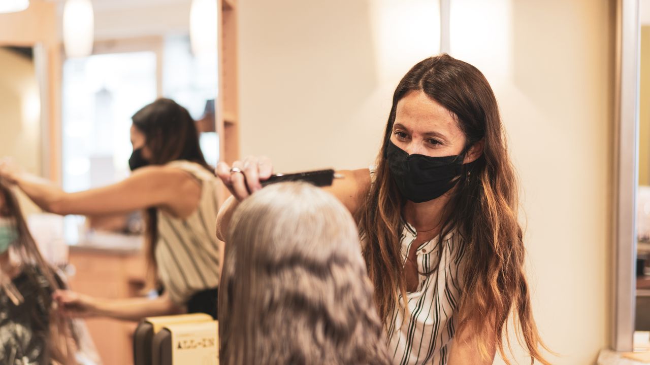 woman having her hair cut by hairdresser wearing face mask