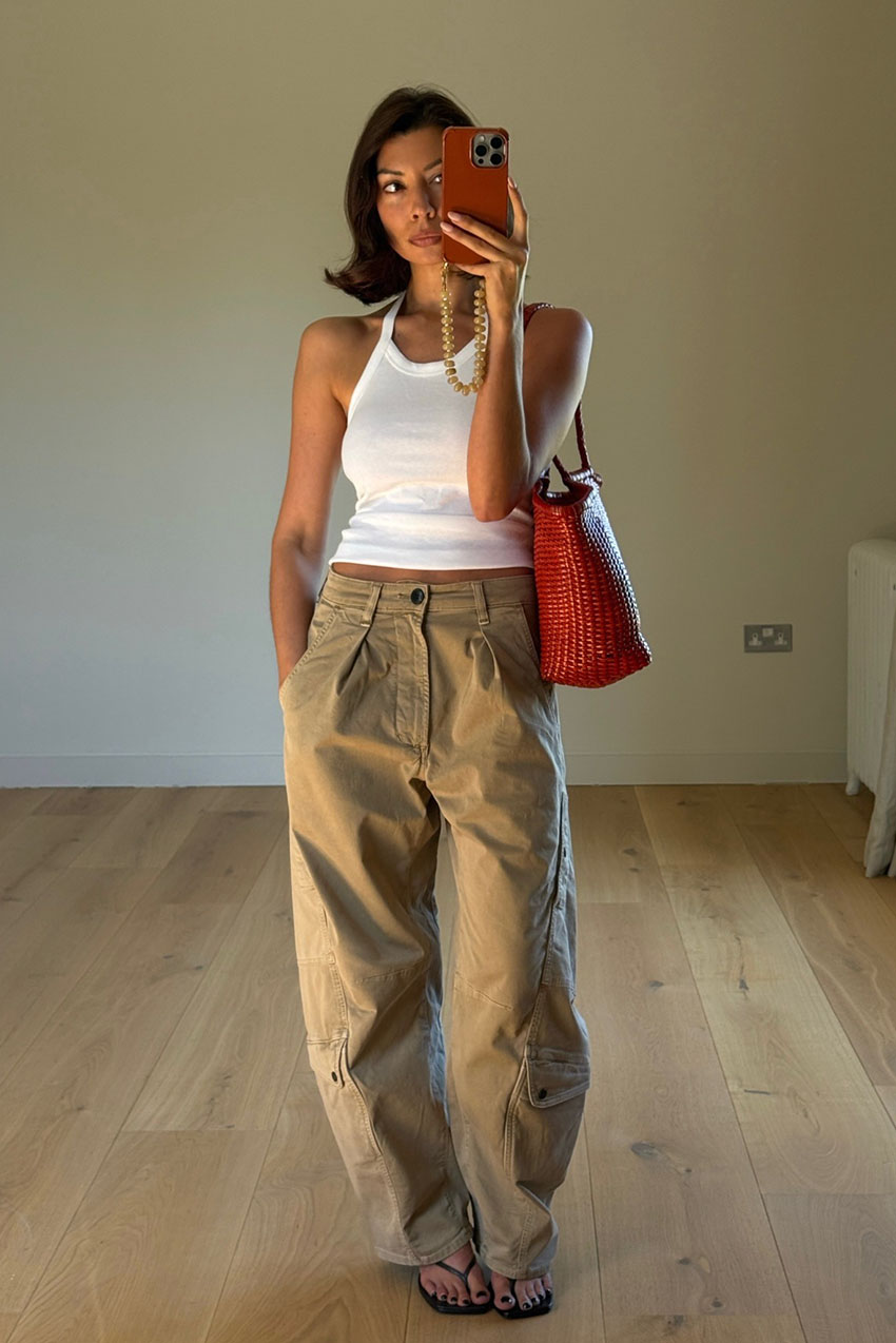 A woman wearing a white tank top, tan cargo pants, a red shoulder bag, and black kitten heel thong sandals.