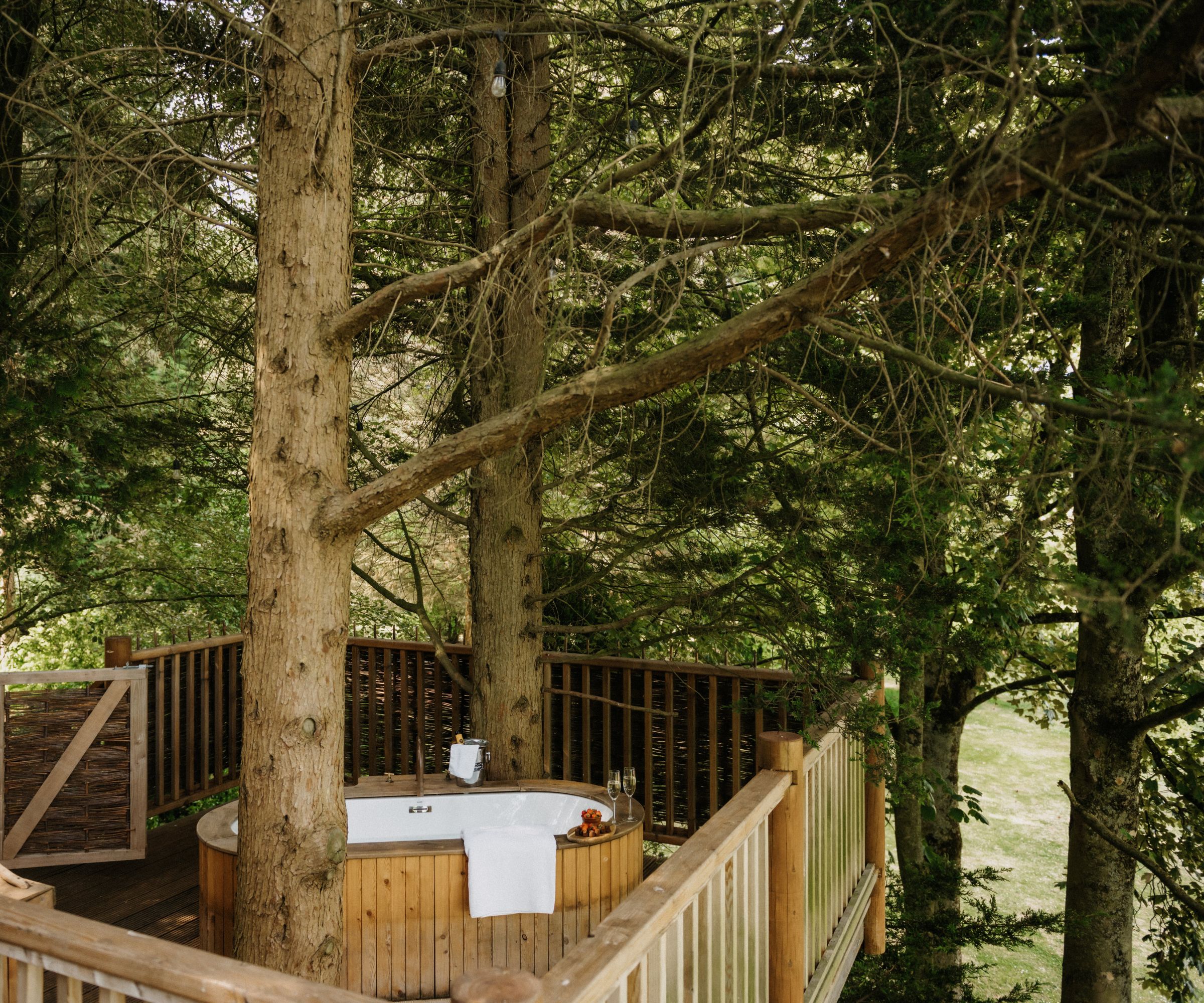 Outdoor freestanding bathtub built into a raised wooden tree deck surrounded by forest greenery.