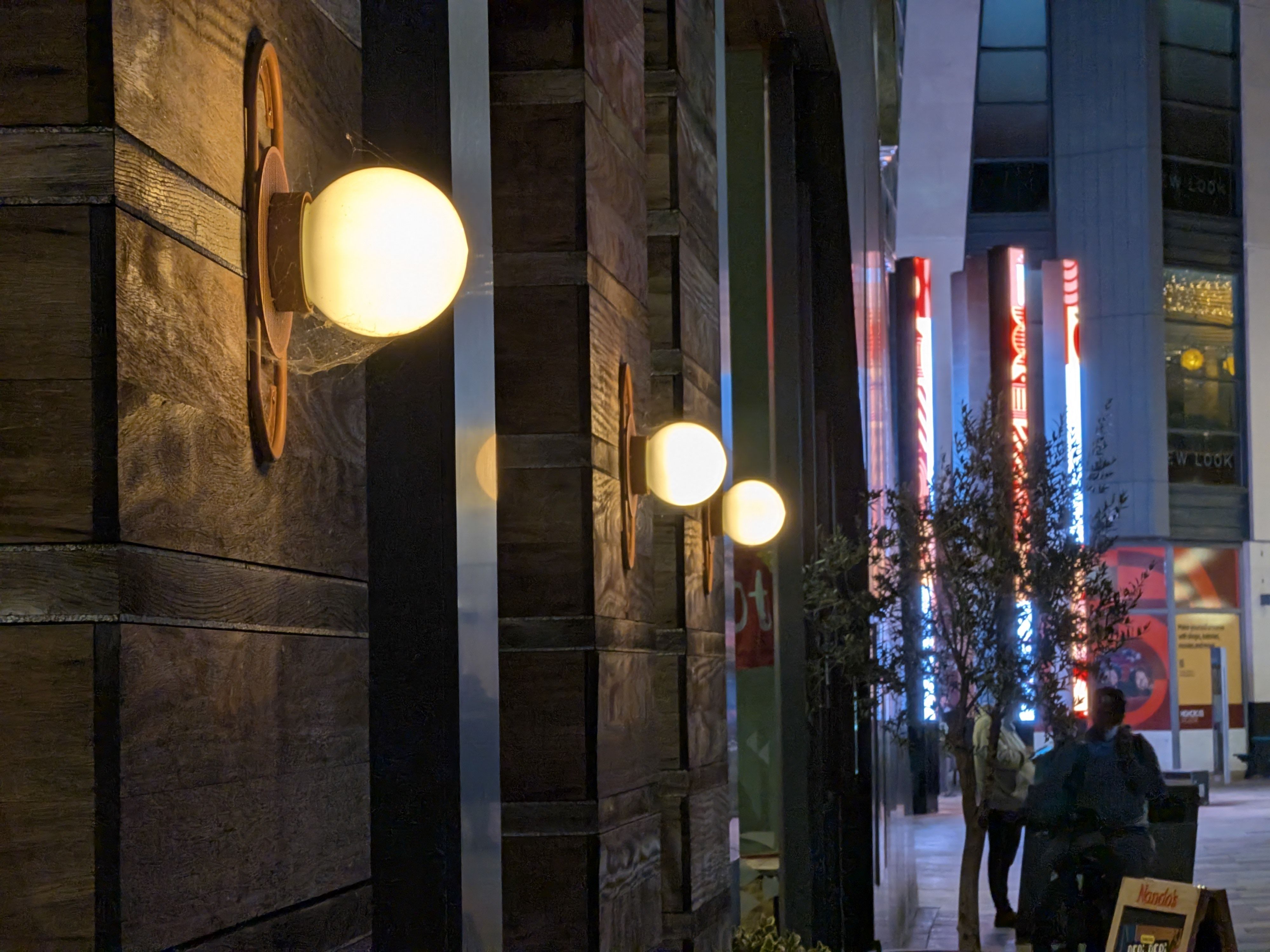 Close-up of a glowing globe wall light mounted on wooden paneling, with colorful city lights blurred in the background.