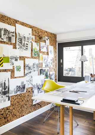 Cork board wall in a home office with wooden floor, a large white desk, and a yellow office chair