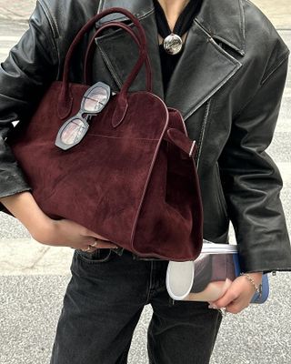 Woman carries burgundy suede Margaux bag by The Row