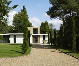 modern house with white render and wood clad finish, gravel driveway lined with trees and lawn