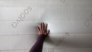 Hand resting on surface of Saatva memory foam hybrid mattress