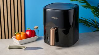 a large black 5.3 quart capacity air fryer with black touchscreen and rose gold embellishments sits upon a brown table with a blue background