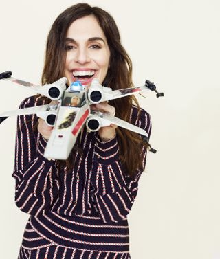 Michelle Rejwan smiles as she holds a toy X-Wing up to the camera