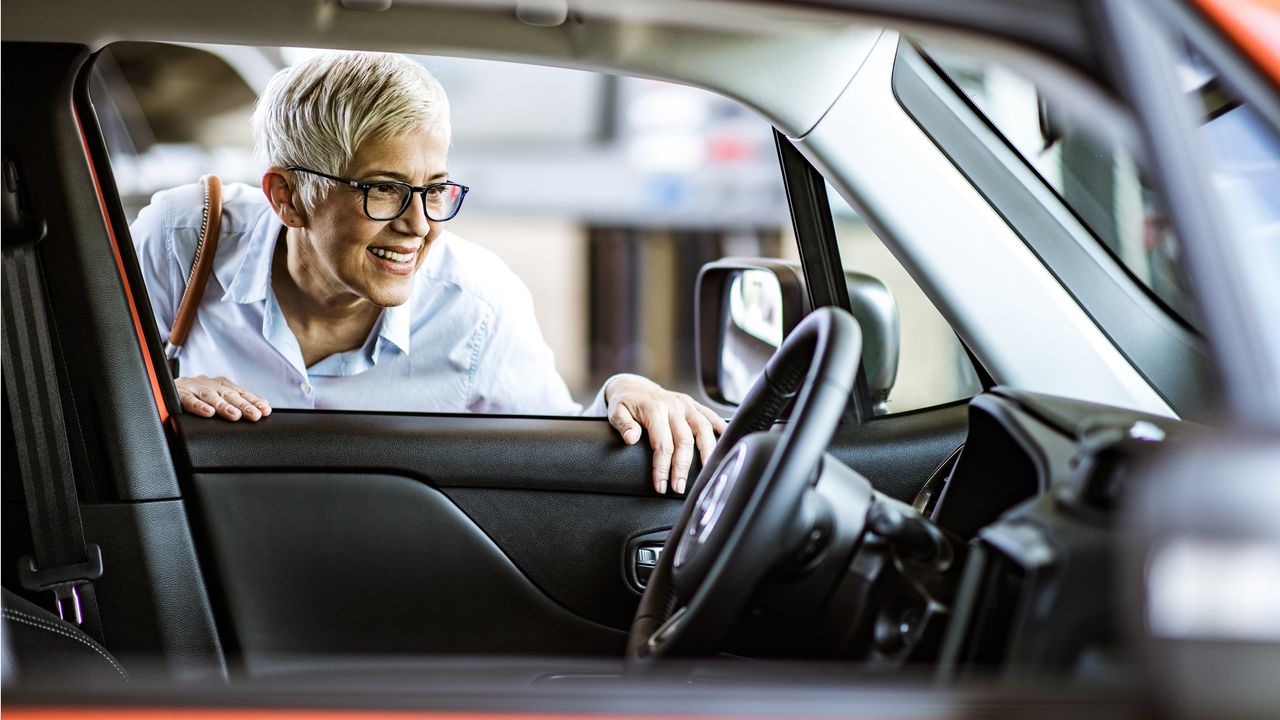 An older woman smiles as she checks out the interior of a new car.