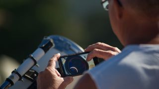 Afocal astrophotography - Rear view of astronomer photographing moon seen through telescope during sunset