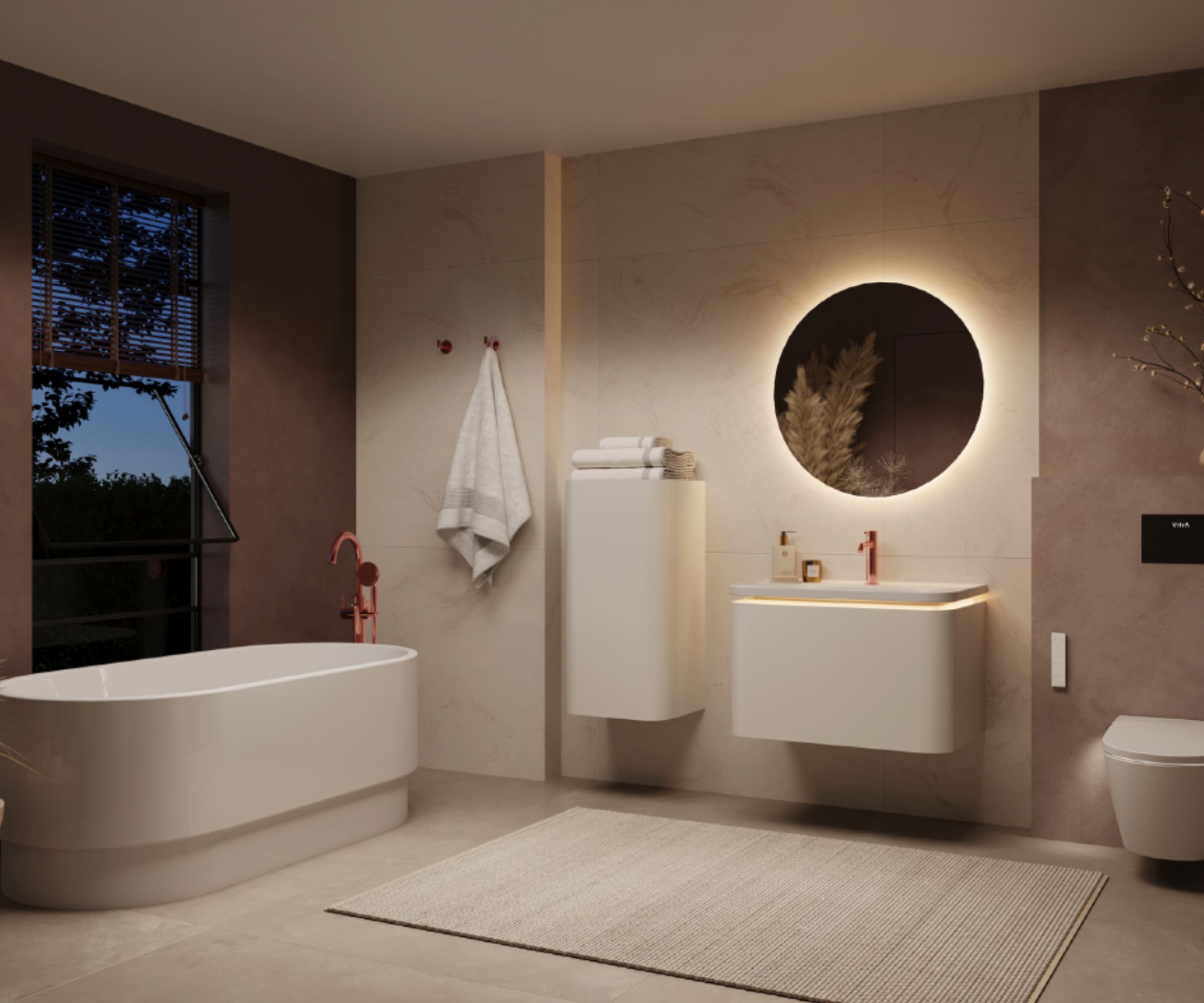 A softly lit, spa-inspired bathroom with warm taupe walls and large-format stone tiles. A white freestanding oval bath with a rose gold floor-mounted tap sits beside a tall window with evening garden views.