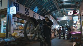 Owen and Yoo Jin ride on a motorbike through a Seoul indoor market in The Recruit season 2