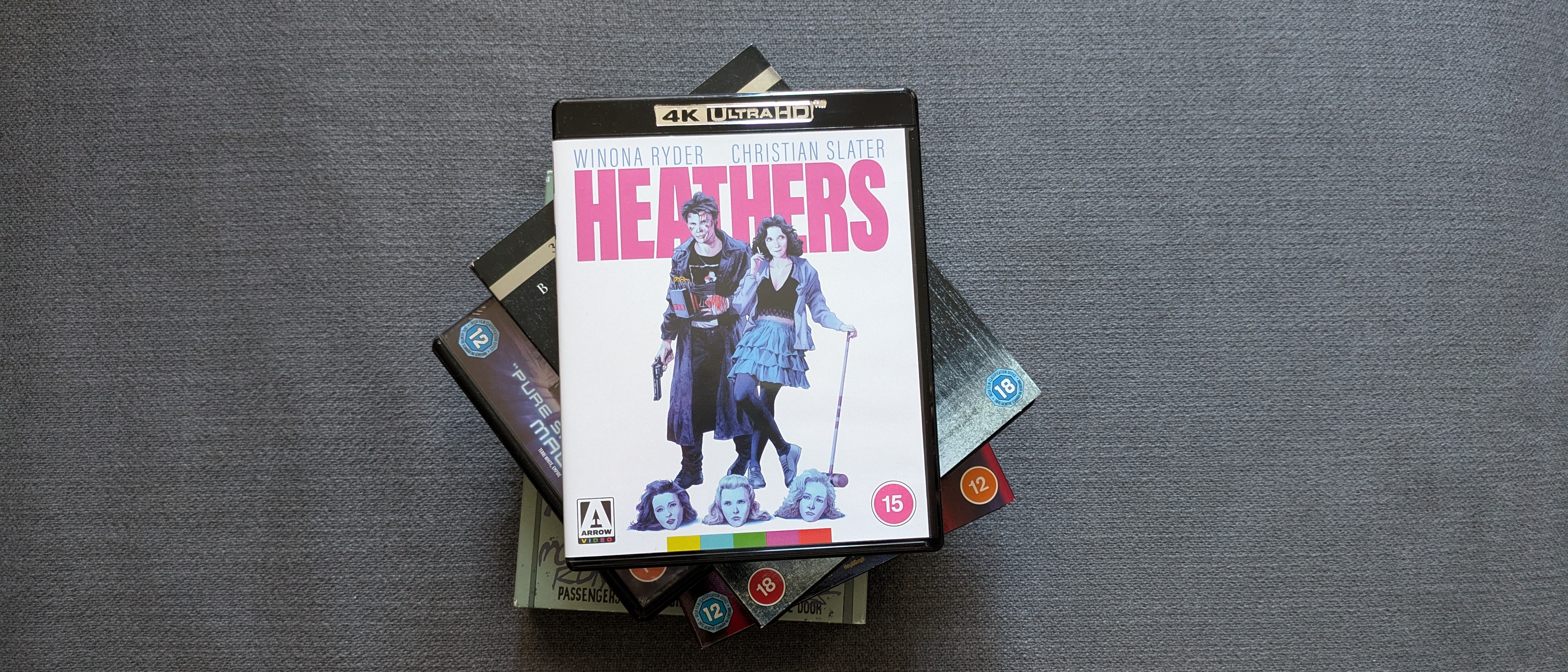 HMV Arrow Films 4K Blu-ray collection hero image with Heathers 4K Blu-ray on a pile of other discs 