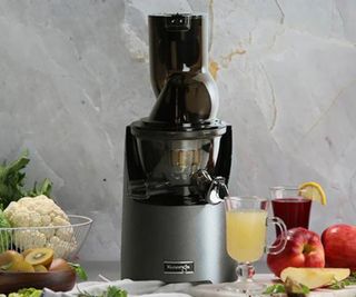 A Kuvings juicer against a gray background, surrounded by fruit.