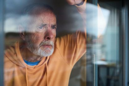 Pensive senior man gazing through the window, wearing a worried expression.